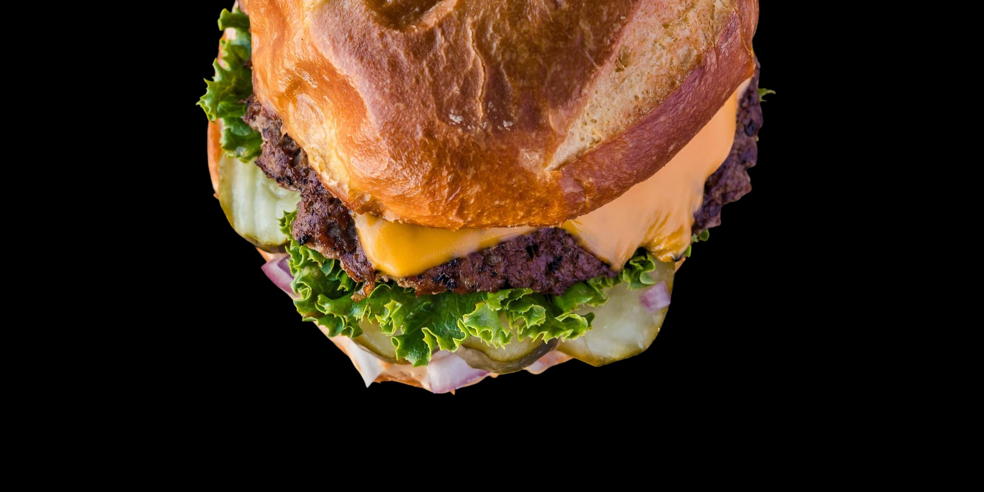 The Classic Fixx — hand-smashed beef patty with American cheese, lettuce, pickles, and SMASH sauce on a pretzel bun, photographed on pure black.